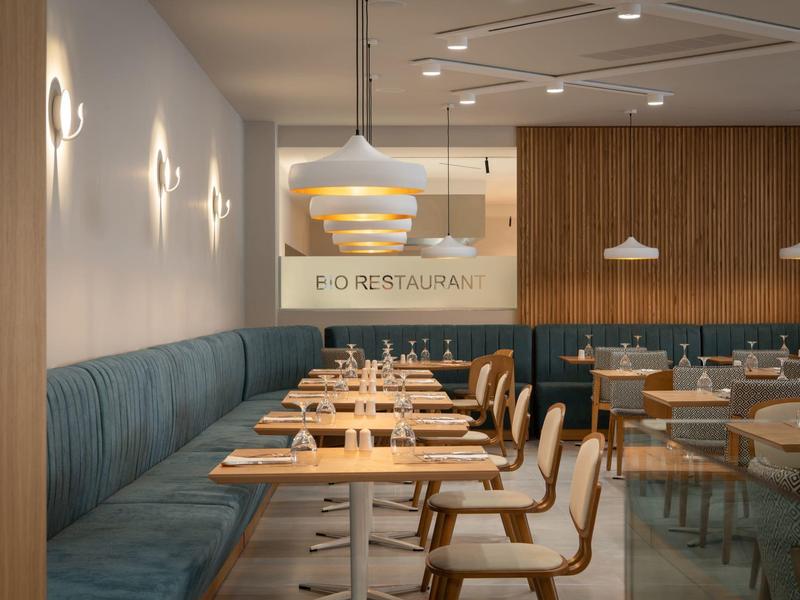 Moderní restaurace s dřevěnými stoly, modrými lavicemi a minimalistickým designem.