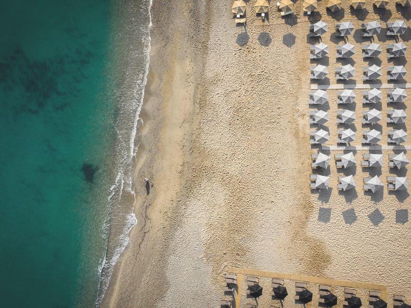 Letecký pohled na pláž s řadami slunečníků a tyrkysovou vodou.