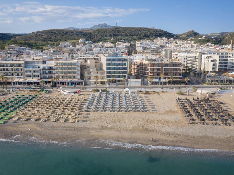 Pláž s řadami slunečníků a lehátek před hotely a kopci v pozadí