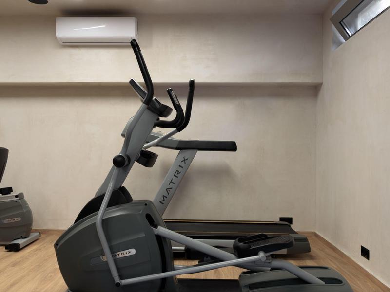 Malá posilovna s běžeckým pásem a eliptickým trenažérem před světlou zdí.