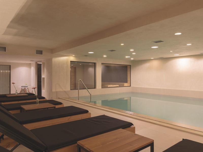 Moderní vnitřní bazén s lehátky v relaxační části hotelu.
