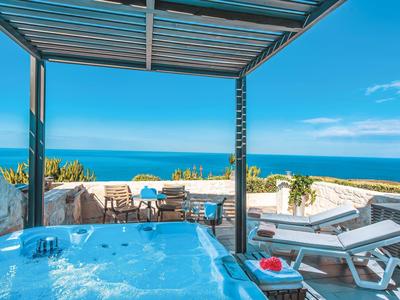 Terrasse mit Whirlpool, Liegestühlen und Meerblick unter blauem Himmel.