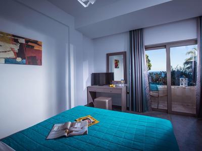 Modernes Schlafzimmer mit türkisfarbenem Bett, Spiegelkommode, Fernseher und Balkon mit Glasfenstern.