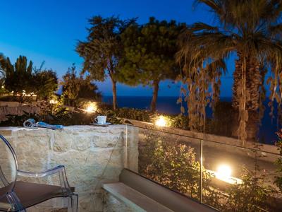 Terrassenbereich mit Stühlen, Steinmauer und Palmen bei Dämmerung am Meer.