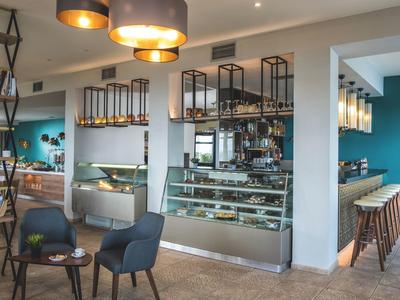 Modernes Café mit blauen Stühlen, Holztischen, Hängelampen und Tresen mit Glasvitrinen.