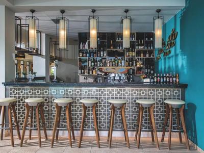 Moderne Hotelbar mit dekorativem Tresen, Hockern und hängenden Lampen vor gut bestücktem Regal.