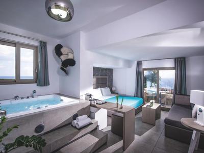Modernes Hotelzimmer mit Badewanne, Doppelbett, Sitzbereich und Meerblick durch große Fenster.