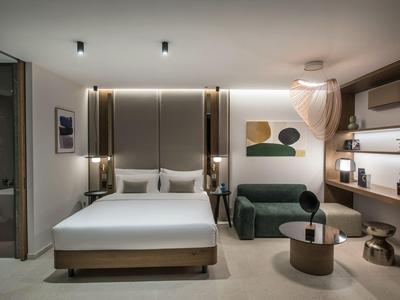 Modernes Schlafzimmer mit großem Bett, grünem Sofa, runden Tischen und minimalistischer Dekoration.