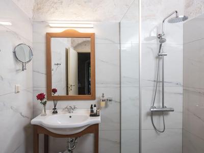 Helles Badezimmer mit weißer Marmorfliese, Waschbecken, Holzspiegel und Dusche mit Glastür.