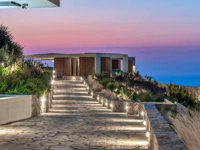 Moderner Weg mit Treppen und Beleuchtung führt zu flachem Haus am Meer, Abendhimmel in Rosa und Blau.