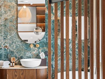 Modern hotel bathroom area with sink, wooden fixtures, and green marble wall