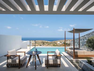 Modern outdoor area with pool, two armchairs, and a view of the sea under blue sky.