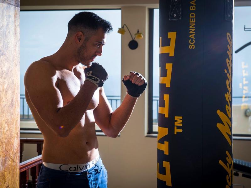 Man trains in a bright room with punching bag and boxing gloves.