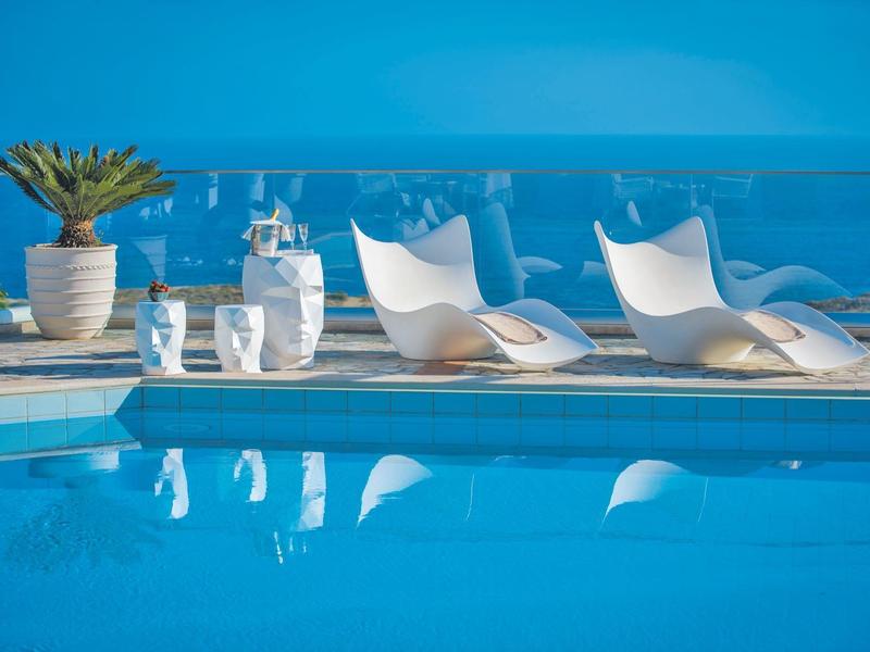 Modern white lounge chairs and decor by the pool with ocean view under clear sky.