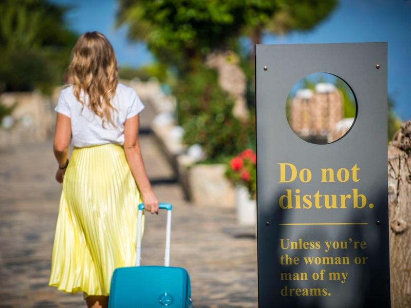 Woman with blue suitcase at a hotel with 'Do not disturb' sign