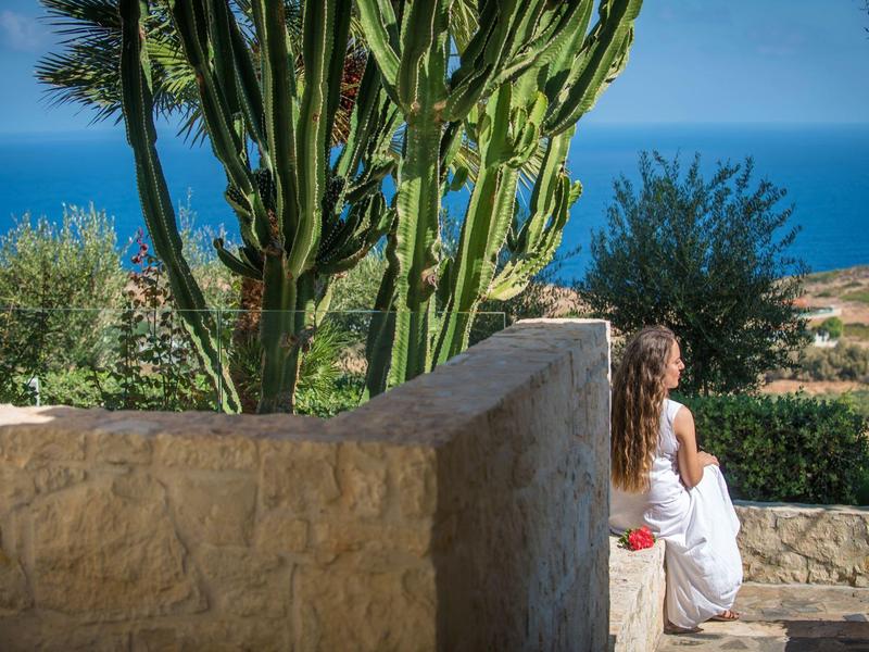 Woman sits on stone wall overlooking sea and cactus in sunny landscape