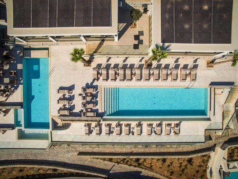 Aerial view of a modern hotel pool with sun loungers and shading plants.