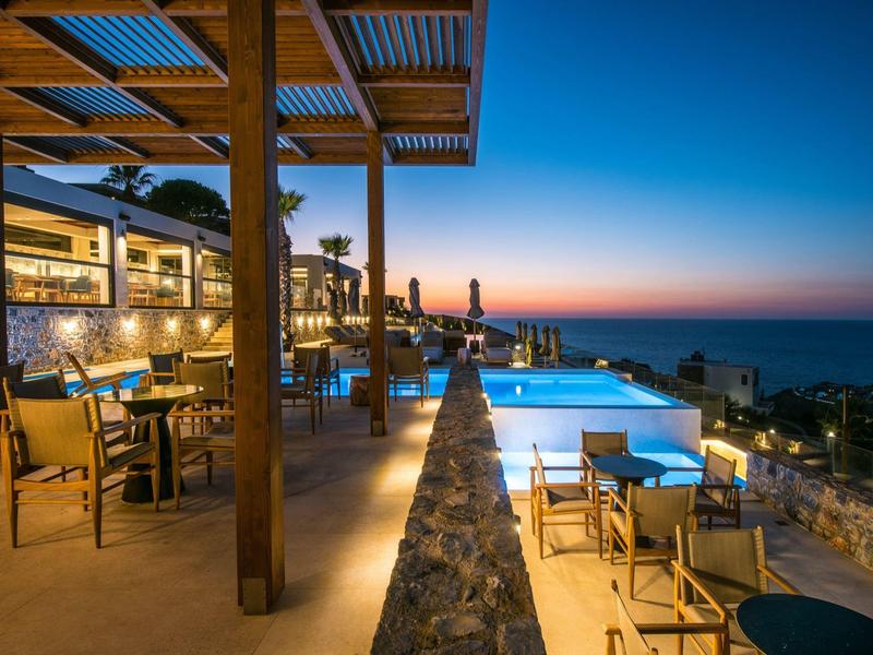 Modern hotel outdoor area with pool and seating at sunset by the sea.
