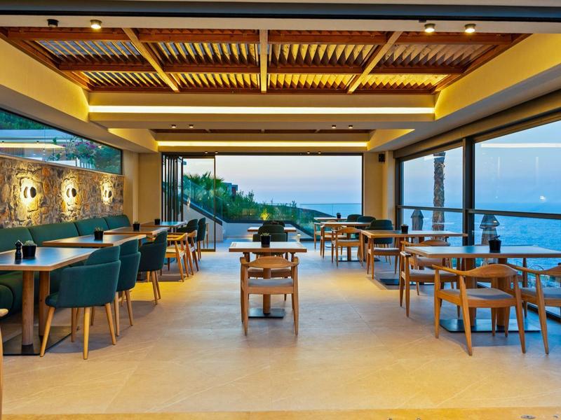 Modern dining area with wooden ceiling and large windows overlooking the sea.
