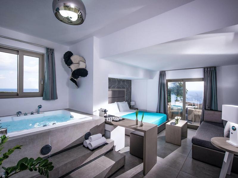 Modern hotel room with whirlpool, bed, sofa, and sea view through large windows