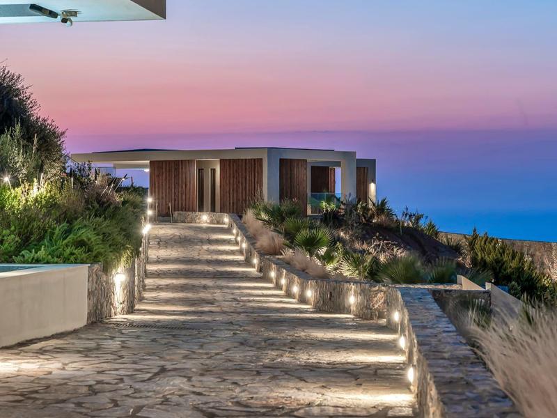 Modern bungalow on a cliff with illuminated pathway and sea view at sunset.