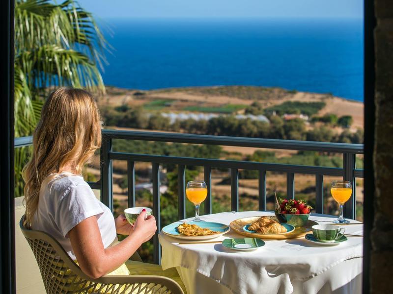 Woman sits on balcony with sea view enjoying breakfast in sunny weather.