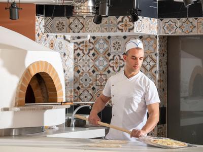 Chef prépare une pizza dans une cuisine moderne avec four en pierre.