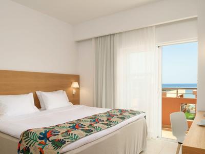 Chambre d'hôtel lumineuse avec lit double, lampe de chevet et balcon avec vue sur la mer.