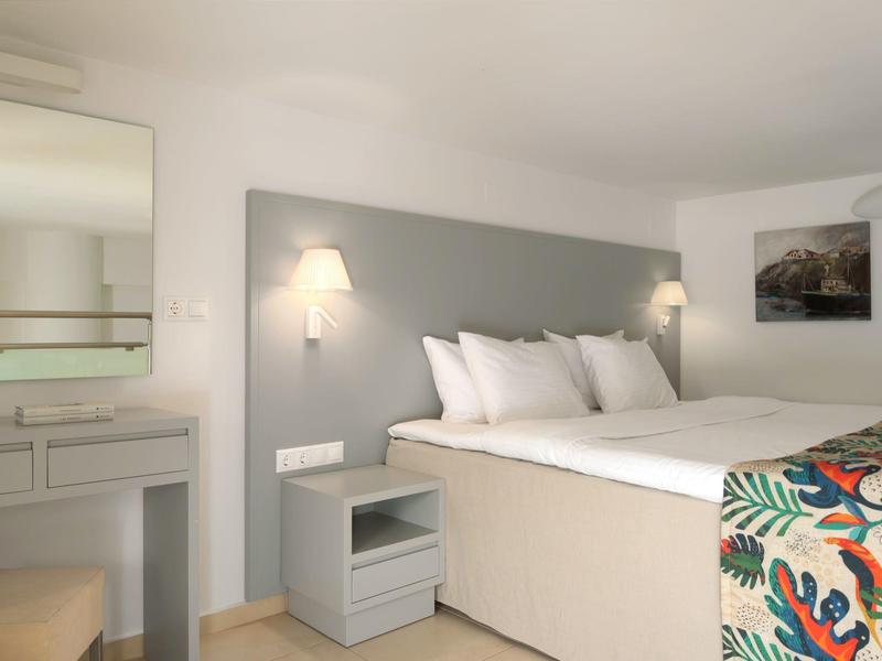 Przytulny pokój hotelowy z podwójnym łóżkiem, stolikami nocnymi, lampkami ściennymi i toaletką z lustrem.