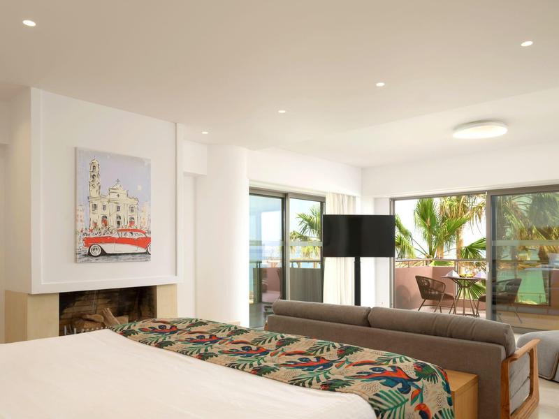 Nowoczesny pokój hotelowy z dużym łóżkiem, kwiecistą pościelą, sofą i balkonem z widokiem na wodę.