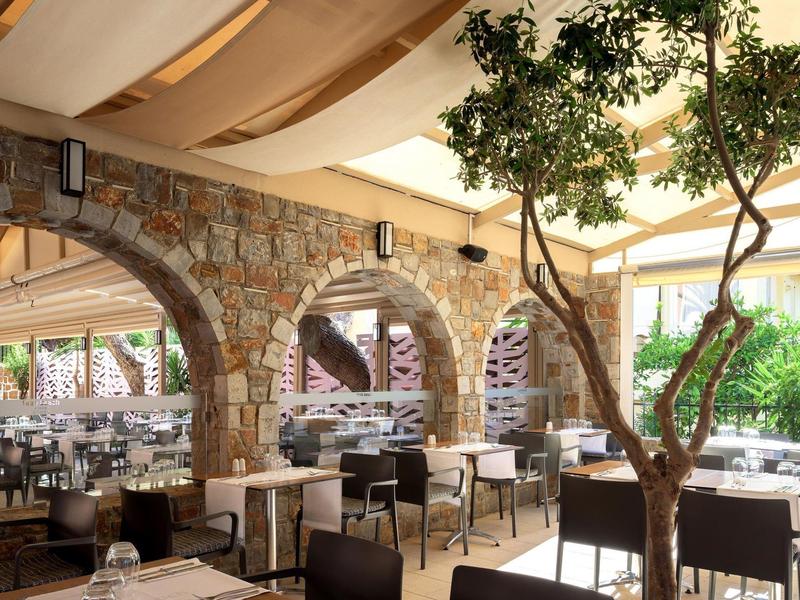 Przestronna restauracja z kamiennymi łukami, wieloma stolikami i drzewem pod kremowym baldachimem.