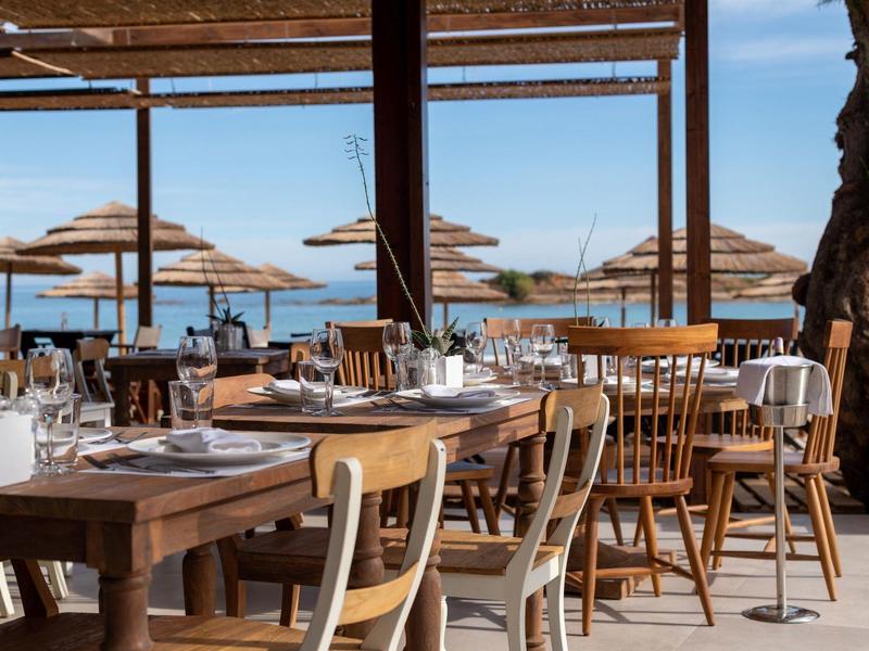 Zewnętrzne miejsce do siedzenia z drewnianymi krzesłami i stołami pod cieniem przy plaży.