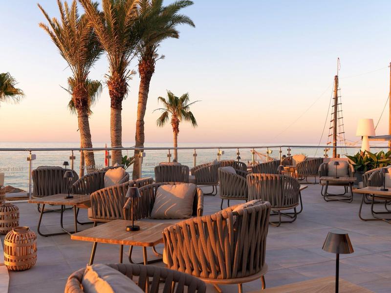 Zewnętrzny salon z wiklinowymi krzesłami i stołami przy palmach o zachodzie słońca.