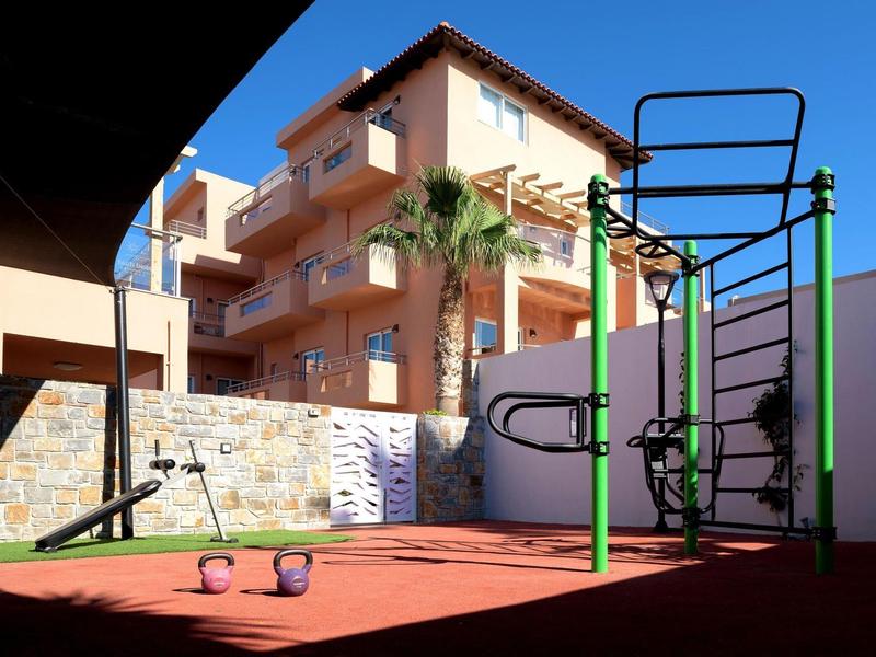 Sprzęt do ćwiczeń na świeżym powietrzu i ciężary na czerwonej macie przy różowym budynku hotelu.