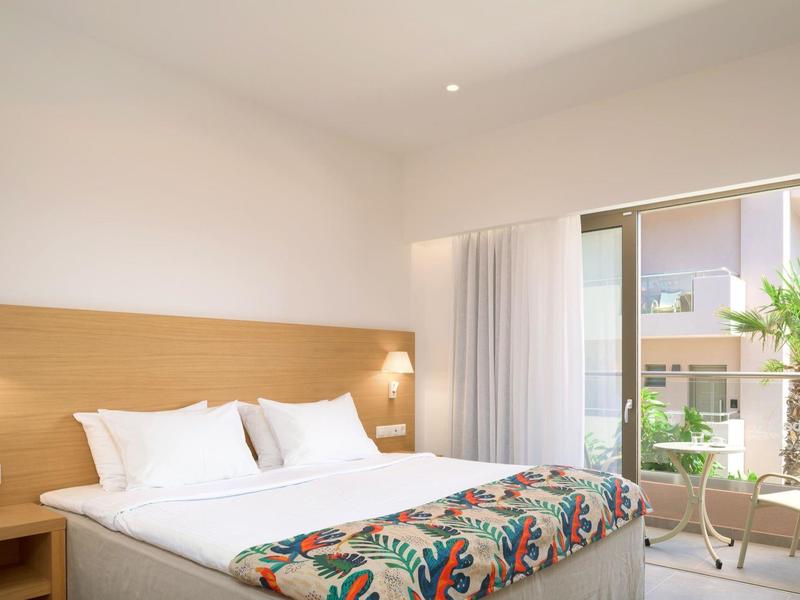 Jasny pokój hotelowy z podwójnym łóżkiem i przesuwnymi drzwiami na balkon z krzesłami na zewnątrz