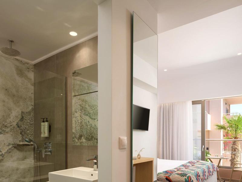 Nowoczesna łazienka połączona z jasną sypialnią z balkonem i tropikalnymi roślinami.