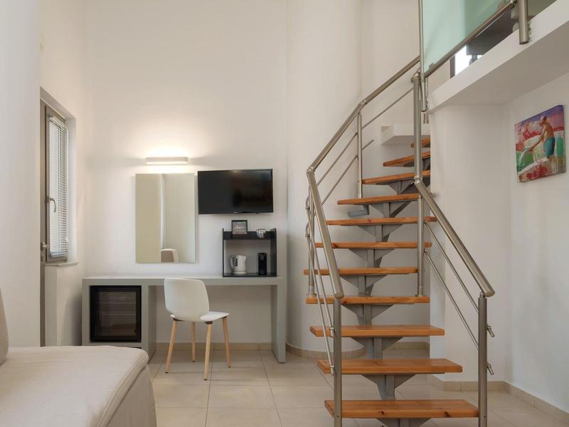 Nowoczesny pokój z drewnianymi schodami, biurkiem, telewizorem i małą lodówką.