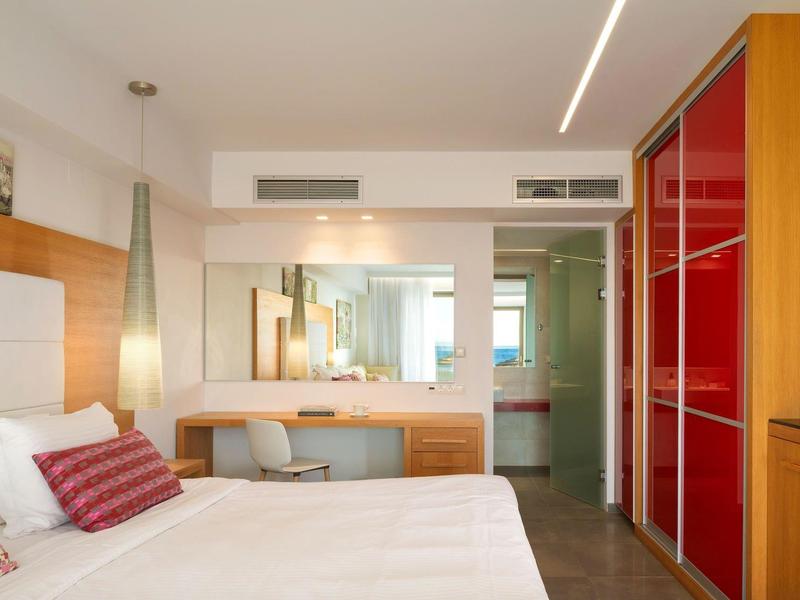 Jasny, nowoczesny pokój hotelowy z wygodnym łóżkiem, drewnianymi meblami i dużym lustrem.