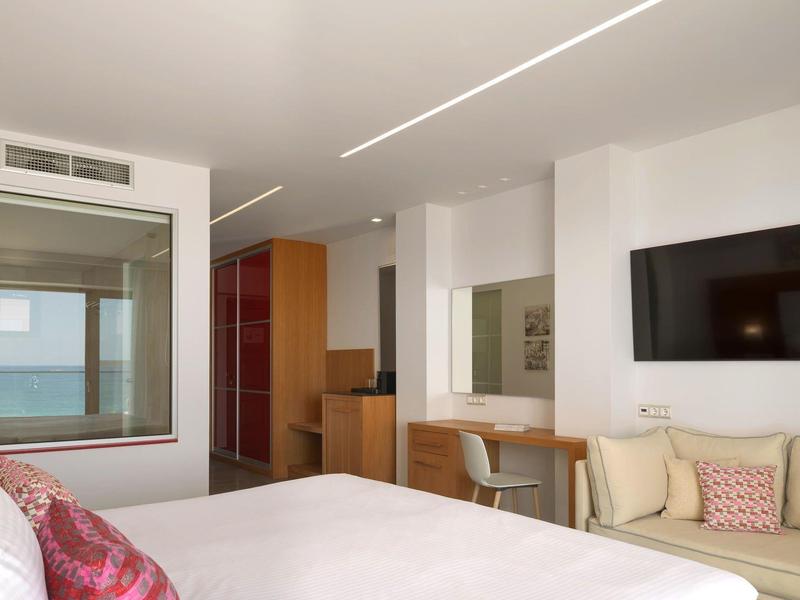 Nowoczesny pokój hotelowy z łóżkiem, przeszklonym prysznicem, telewizorem, sofą i widokiem na ocean.