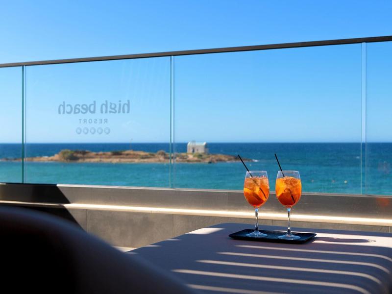 Dwa pomarańczowe koktajle na stole z widokiem na niebieskie morze i odległą wyspę pod czystym niebem.