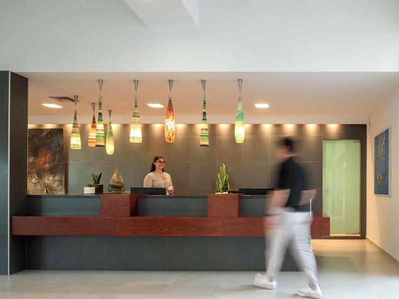 Recepcja hotelu z dwoma pracownikami za ladą i gościem przechodzącym obok.