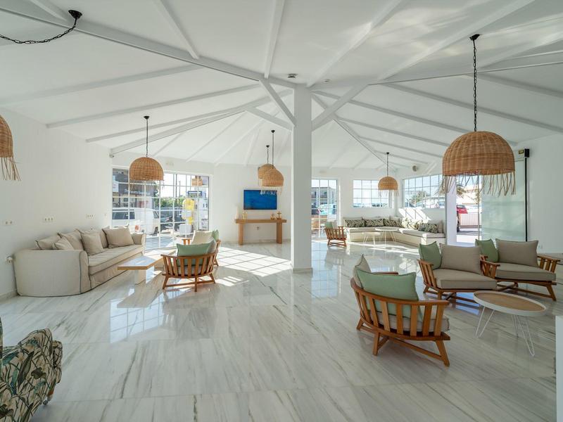 Jasny, przestronny salon z białymi ścianami, drewnianymi meblami i dużymi oknami.