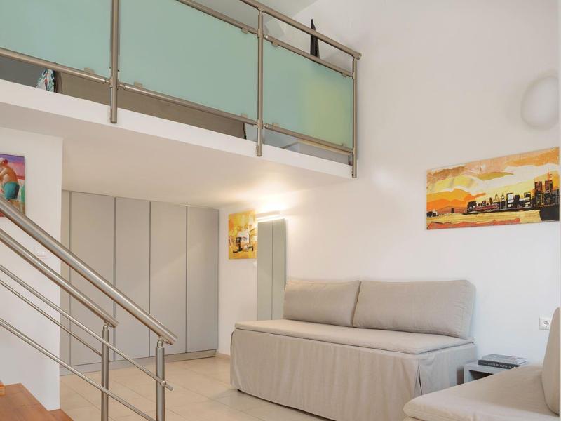 Nowoczesny pokój dzienny z szarą sofą, obrazami na ścianach i metalową balustradą przy schodach.