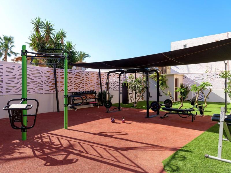 Zewnętrzna siłownia z sprzętem, zieloną trawą i słonecznym, niebieskim niebem.