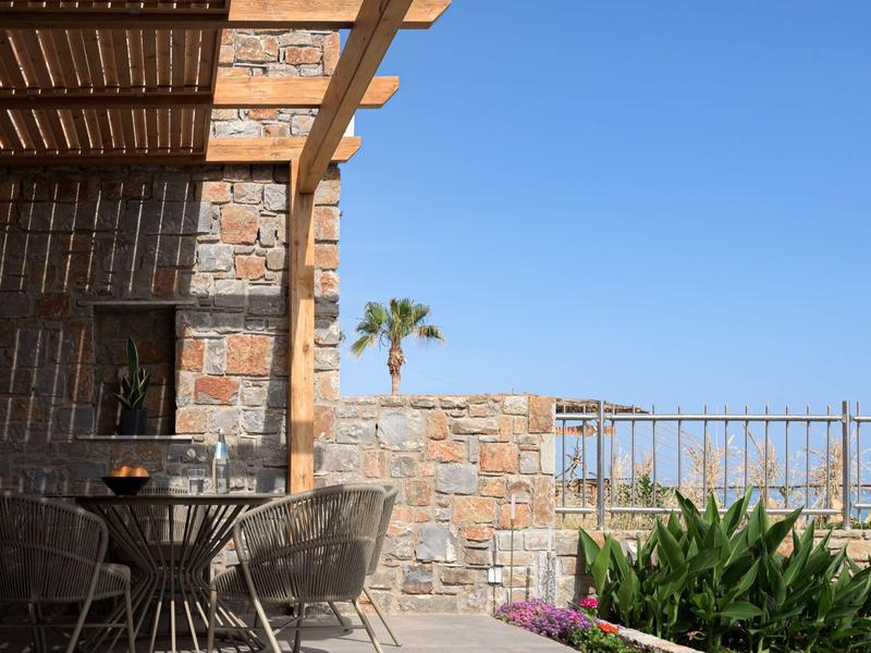 Kamienny taras z krzesłami i stołem, widok na palmę i błękitne niebo.