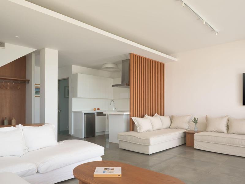 Przestronny salon z beżowymi sofami, drewnianym stolikiem kawowym i nowoczesną kuchnią otwartą.