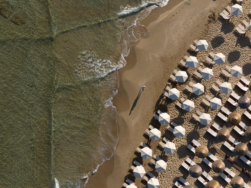 Widok z lotu ptaka na plażę z parasolami i falami morza docierającymi do brzegu.