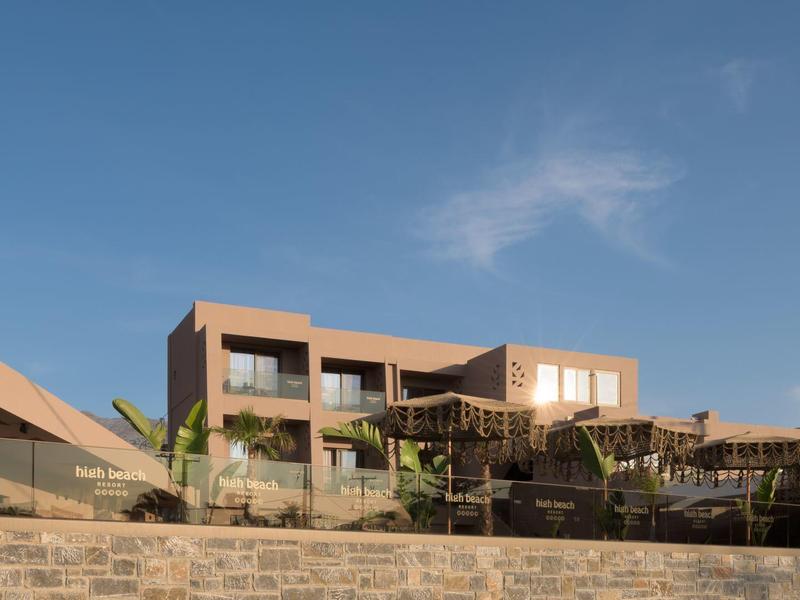 Nowoczesny hotel z balkonami pod czystym niebieskim niebem i palmami na pierwszym planie.