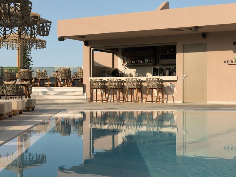 Nowoczesny basen hotelowy z barem, beżowymi meblami i palmami pod czystym niebem.