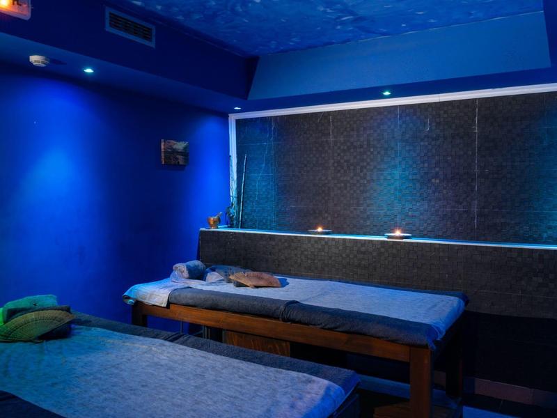 Spokojny pokój spa z niebieskim oświetleniem i wygodnymi łóżkami do masażu.